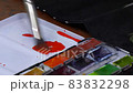 The artist mixes watercolor paints in a palette with a brush. 83832298