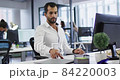 Caucasian businesswoman sitting at desk using laptop and writing notes in notebook in busy office 84220003
