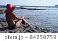 beautiful mature woman in red hat and black bikini calms down looking at the sea 84250759