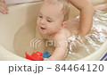 Mother supporting her little baby son palying and swimming in plastic bath at home. Concept of children hygiene, healthcare and parenting. 84464120