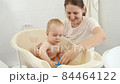Happy smiling mother and baby boy playing with toy boats and ships in small plastic bath. Concept of children hygiene, healthcare and parenting. 84464122