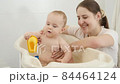 Happy smiling mother looking at her little baby son splashing water and playing in bath. Concept of children hygiene, healthcare and parenting. 84464124