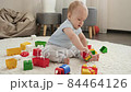 Cute baby boy sitting on carpet and playing with colroful plastic toy car. Concept of children development, education and creativity at home 84464126