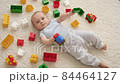 Little smiling baby boy on carpet in playroom covered with colroful toys, bricks and blocks. Concept of children development, education and creativity at home 84464127