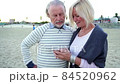 Happy senior man and woman couple sitting together at a table by a beach talking on a cell phone 84520962
