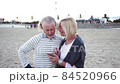 Happy senior man and woman couple sitting together at a table by a beach talking on a cell phone 84520966