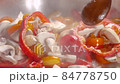 Frying mushrooms champignons in a pan with chunks of red bell pepper and slices of yellow tomatoes. Stirring with a wooden brown spoon 84778750