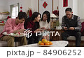 asian mother asking daughter how to play while whole family engaged in exciting mobile game in living room during spring festival. chinese text at back translation: spring and congratulations 84906252