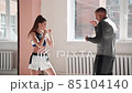 Medium shot of young woman doing boxing workout at the gym and punching her instructor, who is dodging her blows and controlling training process 85104140