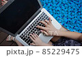Close up typewriting on laptop keyboard near blue swimming pool. 85229475