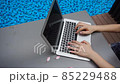 Close up hands typing on laptop keyboard in slow motion near swimming pool. 85229488