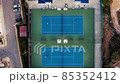 Tennis court aerial view. Slow, top down drone flight over blue outdoor fields with players at practice. Tennis court aerial view. Slow, top down drone flight over blue outdoor fields with players at practice. 85352412