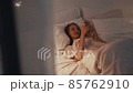 Young woman lying in the bed at night and browsing in her smartphone 85762910