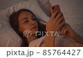Young woman lying in the bed at night and browsing in her smartphone 85764427