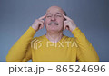 Thoughtful senior man holding fingers on temples standing isolated on blue wall 86524696