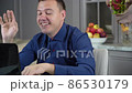 Millenial man greets household off-screen and gestures that he needs to continue his work on laptop 86530179