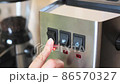 a barista press a finger on the button for turning on an espresso coffee machine. close-up of household appliances made of steel with black buttons. 86570327