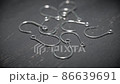 Fish hooks made of light metal are scattered on a gray table in close-up. Background in blur. 86639691