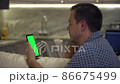Relaxed man looking at smartphone with green screen chroma key display while relaxing on sofa 86675499