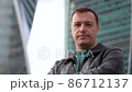 Businessman standing outdoors with office building, looking at camera and shaking head for agreement 86712137