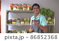 Asian male greengrocer showing vegetables and showing a phone screen 86852368