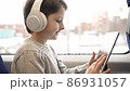 Kid traveling by the train, child watching cartoon or playing games on tablet pc sitting by the window. Schoolboy in a high speed express train on family vacation, Entertainment for young passenger. 86931057