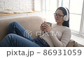 Young ethnic woman chilling on comfortable sofa with closed eyes wearing wireless headphones, asian mixed race girl enjoys listening chill music and audio sound relaxing at home 86931059