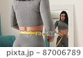 Fitness Woman Measuring body With Tape Standing In Front Of Mirror At Home 87006789