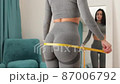 Fitness Woman Measuring body With Tape Standing In Front Of Mirror At Home 87006792