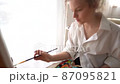 Portrait of a female painter painting a masterpiece in an art workshop. Profile of a girl to draw a picture near the window. Close-up of the face of a concentrated creator. Hobby concept 87095821
