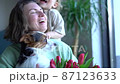 Happy mother on mother's day holds a dog and a bouquet of tulips in her hands while her little son hugs her. Birthday girl or international women's day 87123633