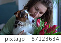 Smiling caucasian woman with a bouquet of tulips kissing her pet dog sitting on floor at home. lifestyle, pet, companionship and animal friendship concept 87123634