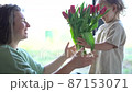 Cute blond boy gives his mother a beautiful fresh bouquet of red tulips. Mother and son, mother's day 87153071