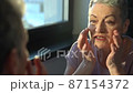 Senior female looking at sagging skin face in mirror, old age appearance. Portrait of senior woman applying anti-aging cream. Portrait of an attractive middle aged woman looking into a mirror 87154372