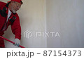 A man paints a wall in poor color with a roller on a long handle. An elderly pensioner in a red overalls makes repairs in his house 87154373