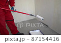 A worker does whitewashing in a new house. Mature man painting walls white while holding white paint roller 87154416
