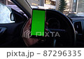 Driver in car holds phone with green screen in city yard 87296335