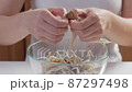 Close-up of a woman's hands dividing fresh mushrooms into fibers and throwing them into dishes 87297498