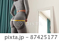 Fitness Woman Measuring body With Tape Standing In Front Of Mirror At Home 87425177