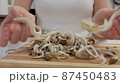 Close-up of a woman's hands dividing fresh mushrooms into fibers and throwing them into dishes 87450483