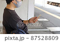 駅のホームでスマートフォンを操作する日本人男性 87528809