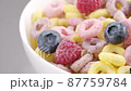 Sliding panoramic front view of milk flow pouring into white bowl with colorful cereal rings and fresh berries 87759784