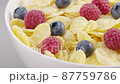 Sliding panoramic front view of milk flow pouring into white cereal bowl with cornflakes, blueberries and raspberries 87759786