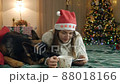 Pretty woman in a warm knitted sweater drinks hot chocolate and relaxes while lying on the bed with his cute dog German Shepherd decorated house with a Christmas tree 88018166