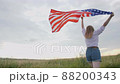 Patriotic young woman holds the US flag and runs across the field 88200343