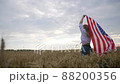 Happy patriotic young woman waves the US flag and jumps into the field 88200356