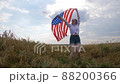 Happy patriotic young woman waves the US flag and jumps into the field 88200366