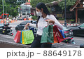A asian young woman sitting on the bench resting after shopping from shopping mall in the park near street. 88649178
