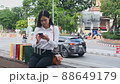 Young asian woman sitting on the bench and using smartphone with paper shopping bags after shopping in the park near street. 88649179