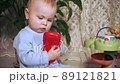 concentrated little girl holds a red toy in her hands and carefully examines it 89121821